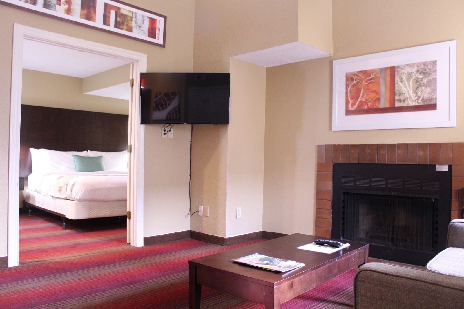 A hotel room with a bed, a flat-screen TV mounted on the wall, a fireplace, and a coffee table.