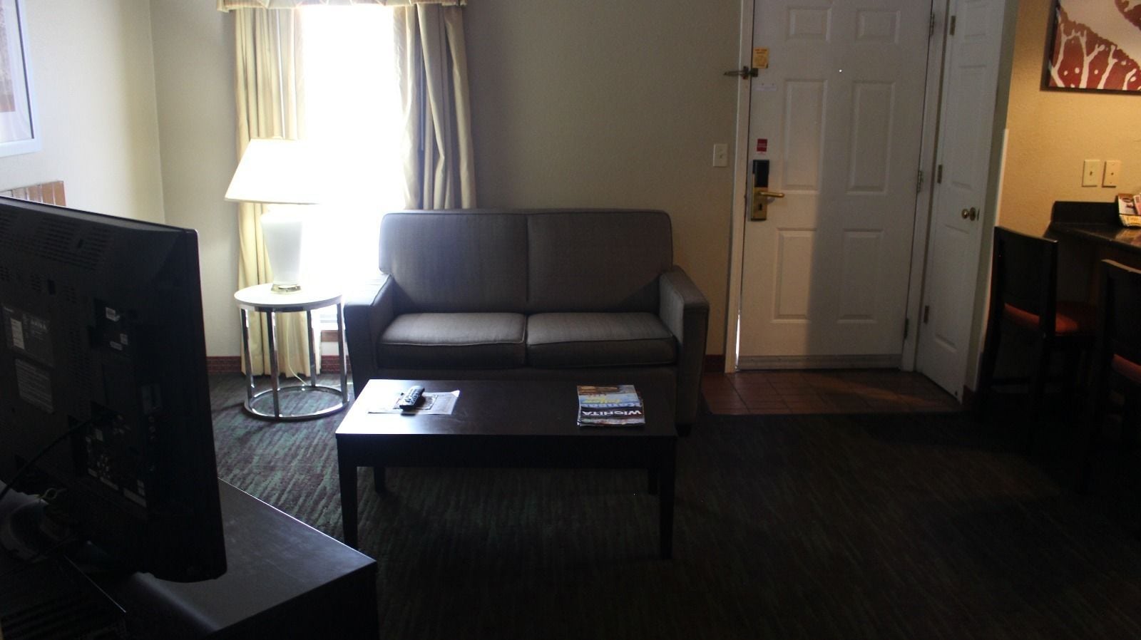 A hotel room with a sofa, a coffee table with a magazine, a TV, and a lamp.