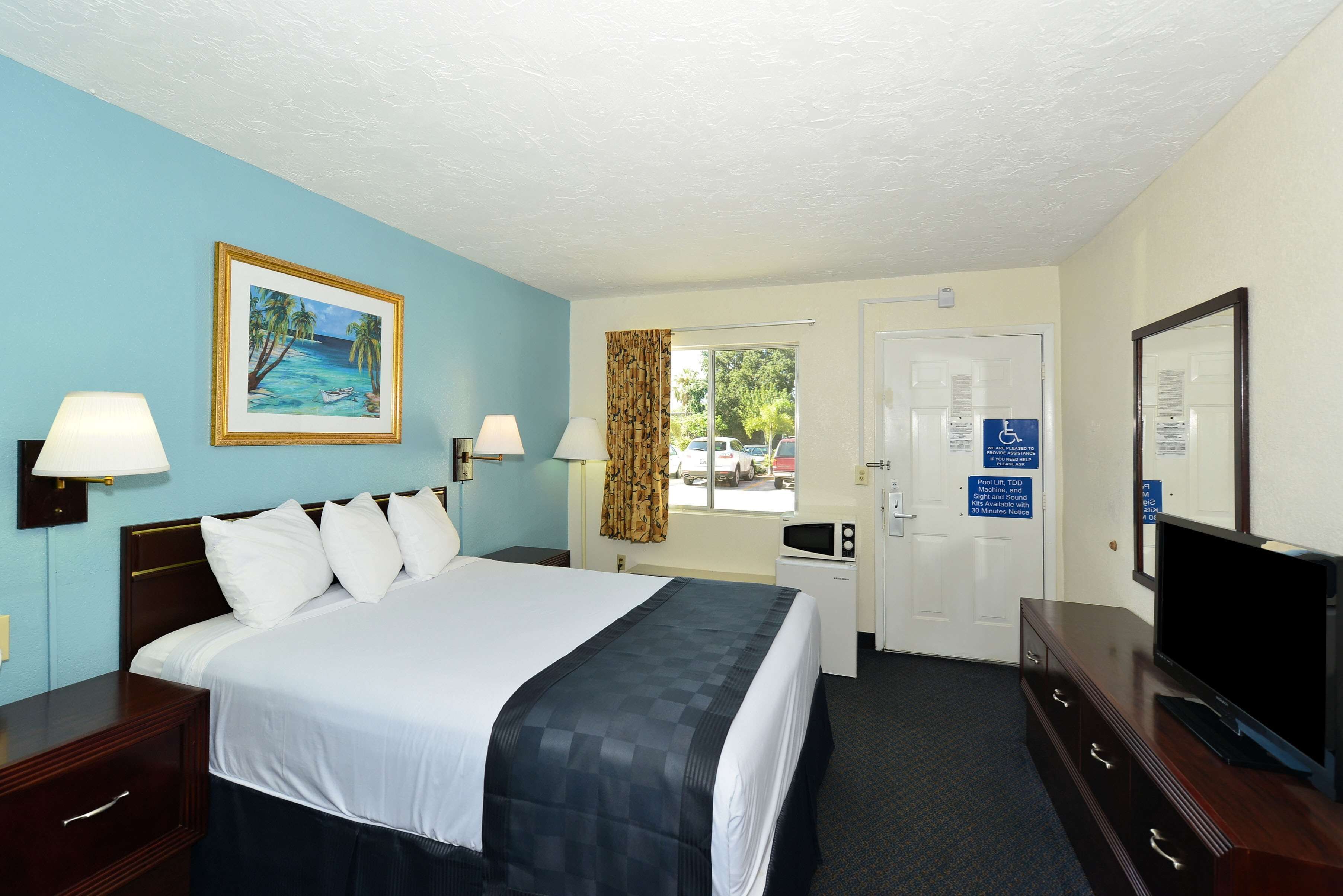 A hotel room with a bed, bedside lamps, a television, a desk, and a window with a view of the outside.