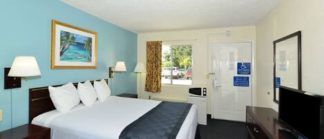A hotel room with a bed, bedside lamps, a television, a desk, and a window with a view of the outside.