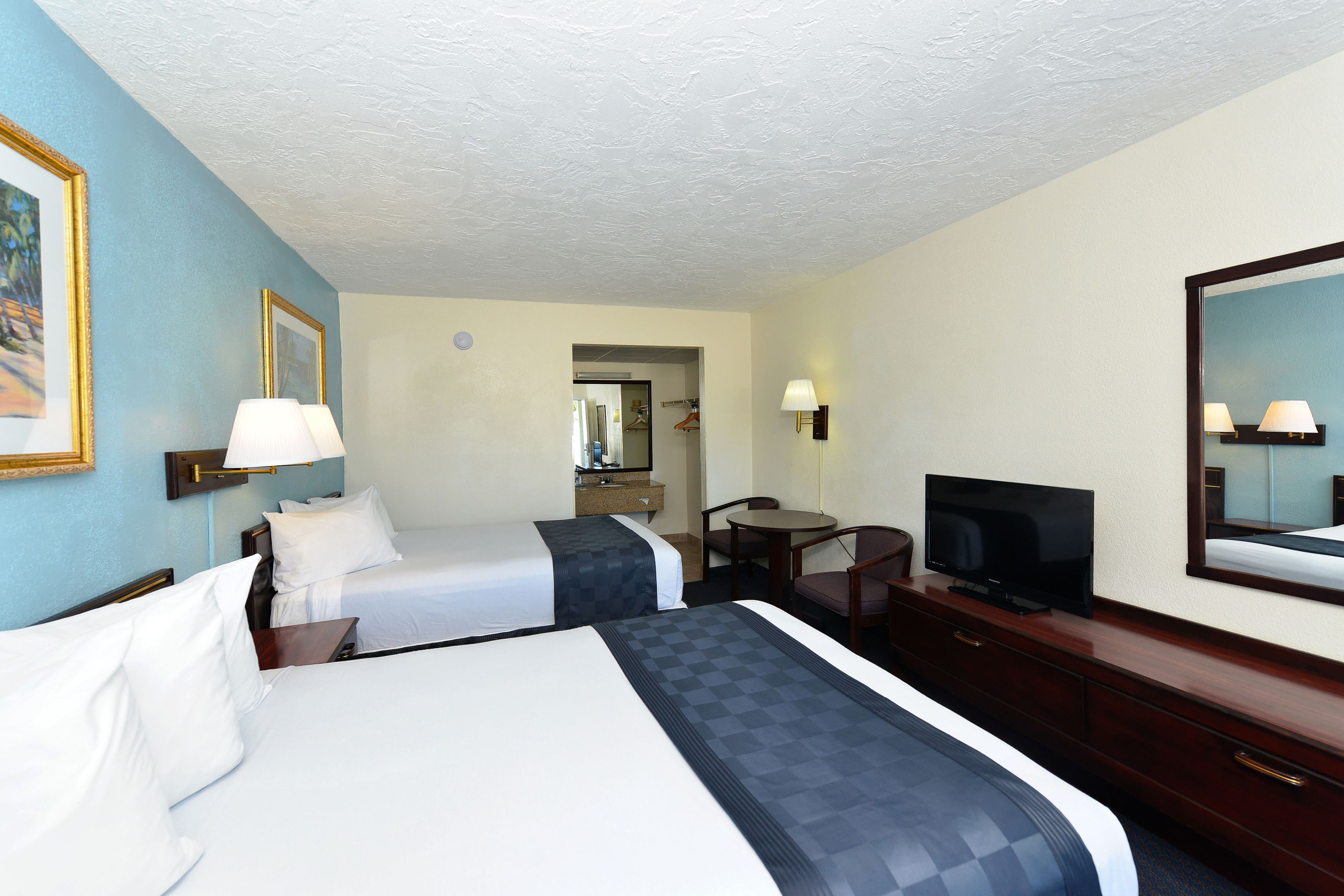 Een hotelkamer met twee bedden, een bureau met een televisie, een stoel en een spiegel.