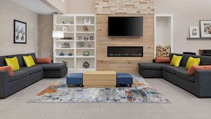 A modern living room with two grey sofas, a wooden coffee table, and a colorful rug. There is a TV mounted on the wall and a fireplace below it.