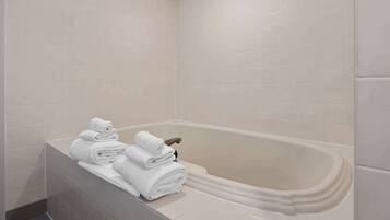 A bathroom with a bathtub, tiled walls, and a stack of neatly folded white towels on the edge.