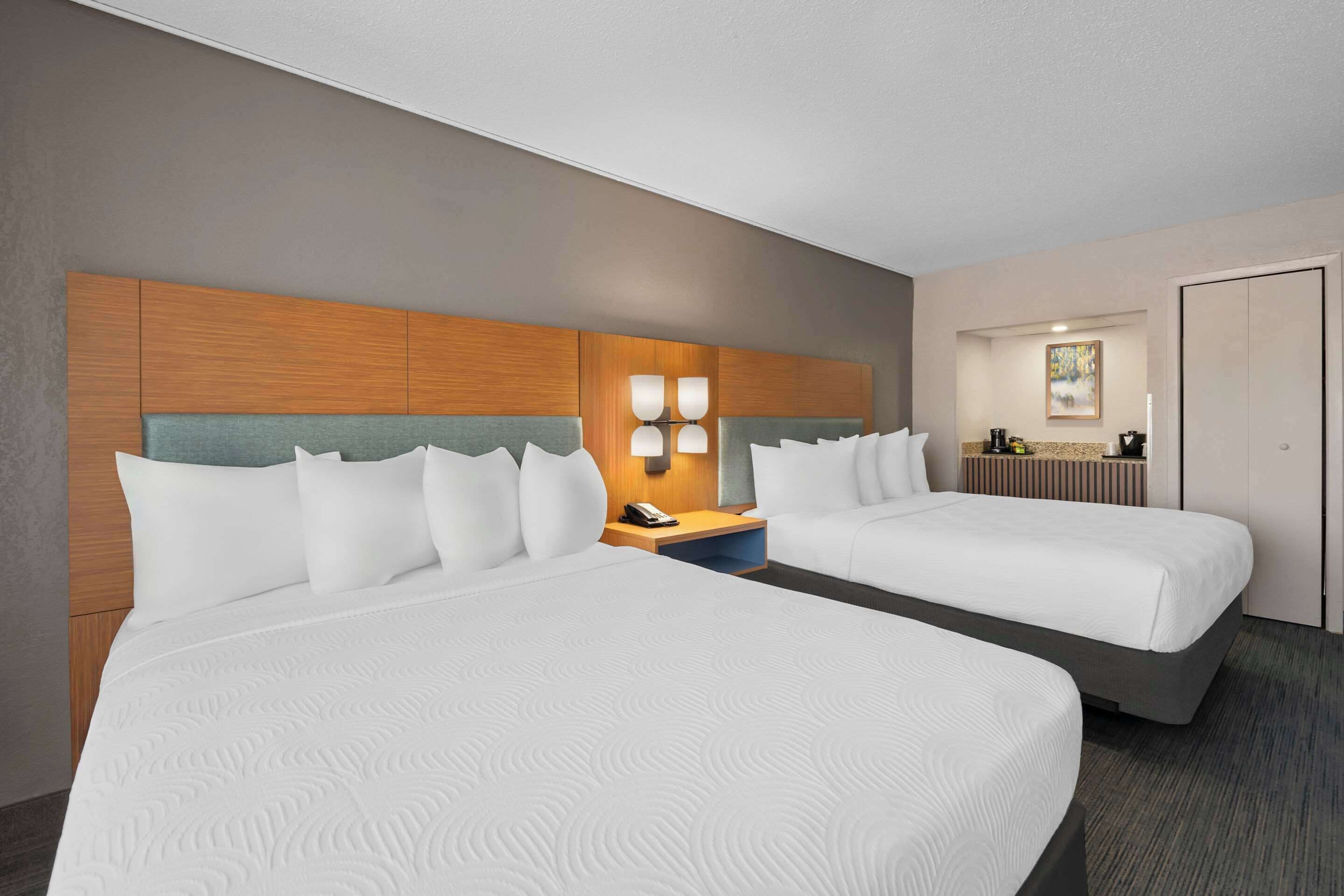 A hotel room with two beds, a wooden headboard, bedside lamps, a nightstand, and a painting on the wall.