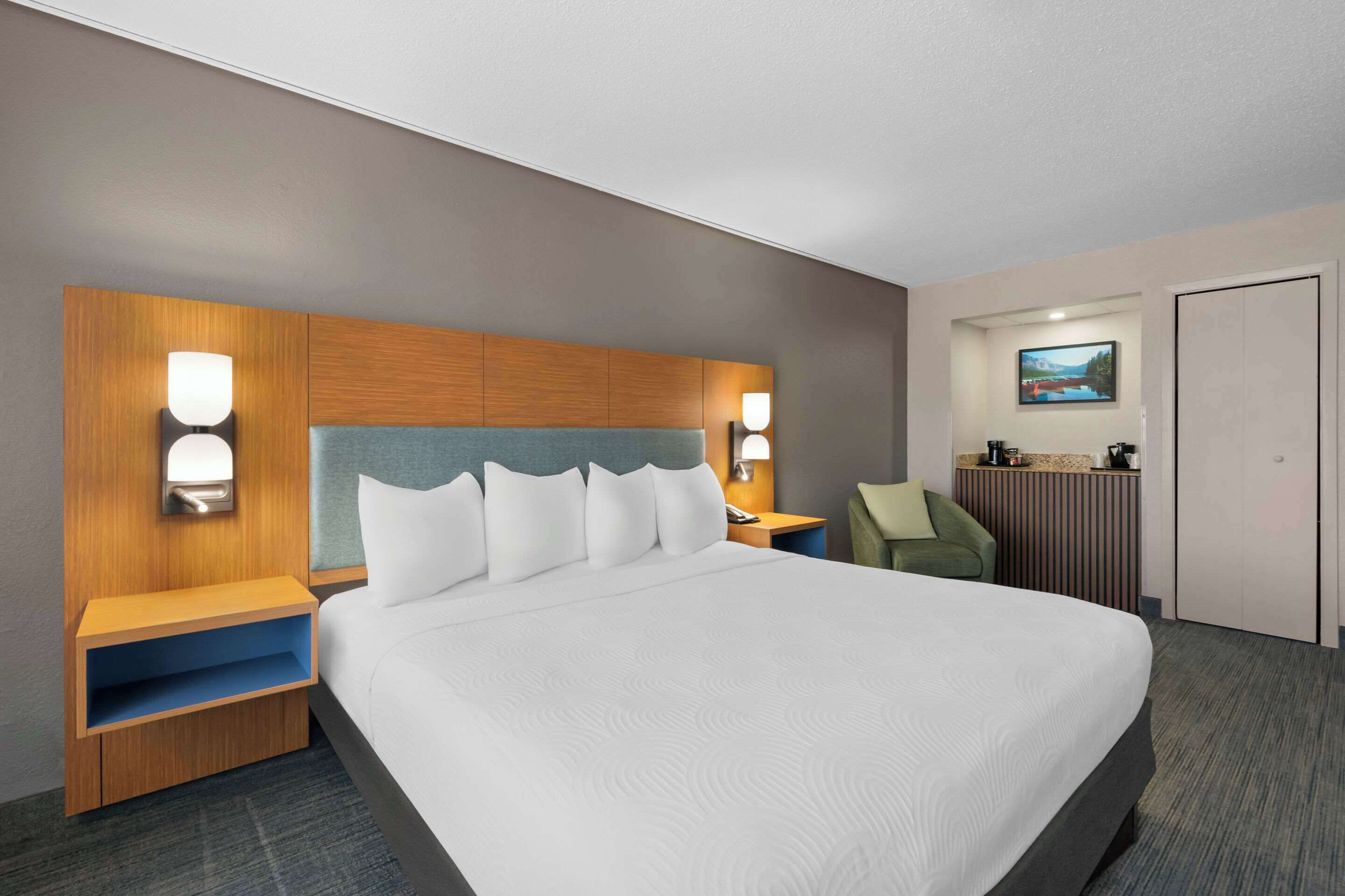 A hotel room with a large bed, wooden headboard, bedside tables with lamps, a small desk, and a chair.