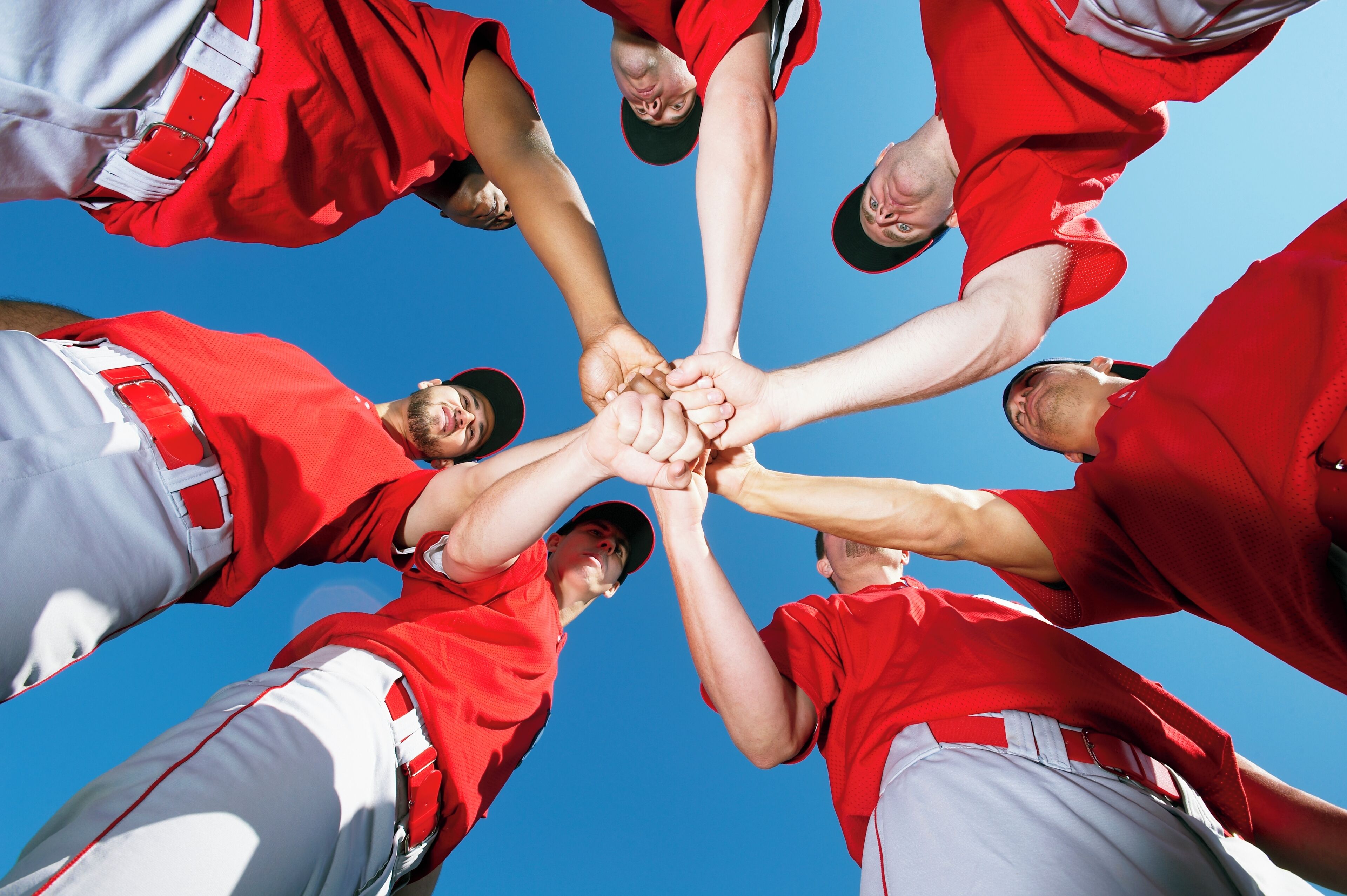 Un grupo de personas con uniformes deportivos rojo y blanco forman un círculo uniendo sus manos.