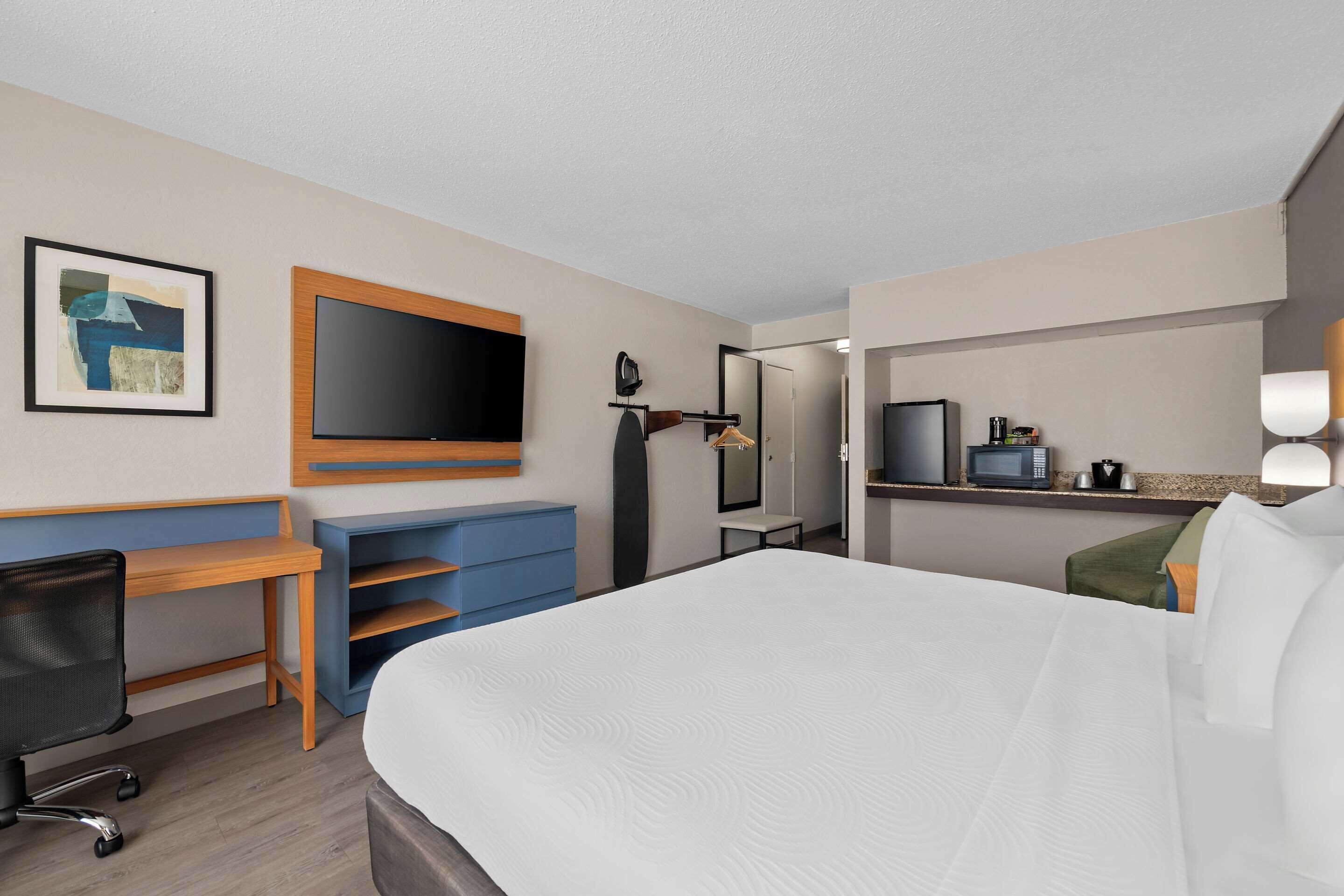 A hotel room with a large bed, a desk, a chair, a television, a microwave, and a coffee machine.