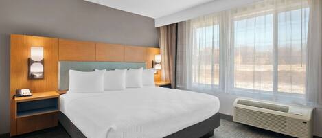 Habitación de hotel con una cama grande, cabecera de madera, lámparas de noche, un teléfono y una ventana con cortinas.