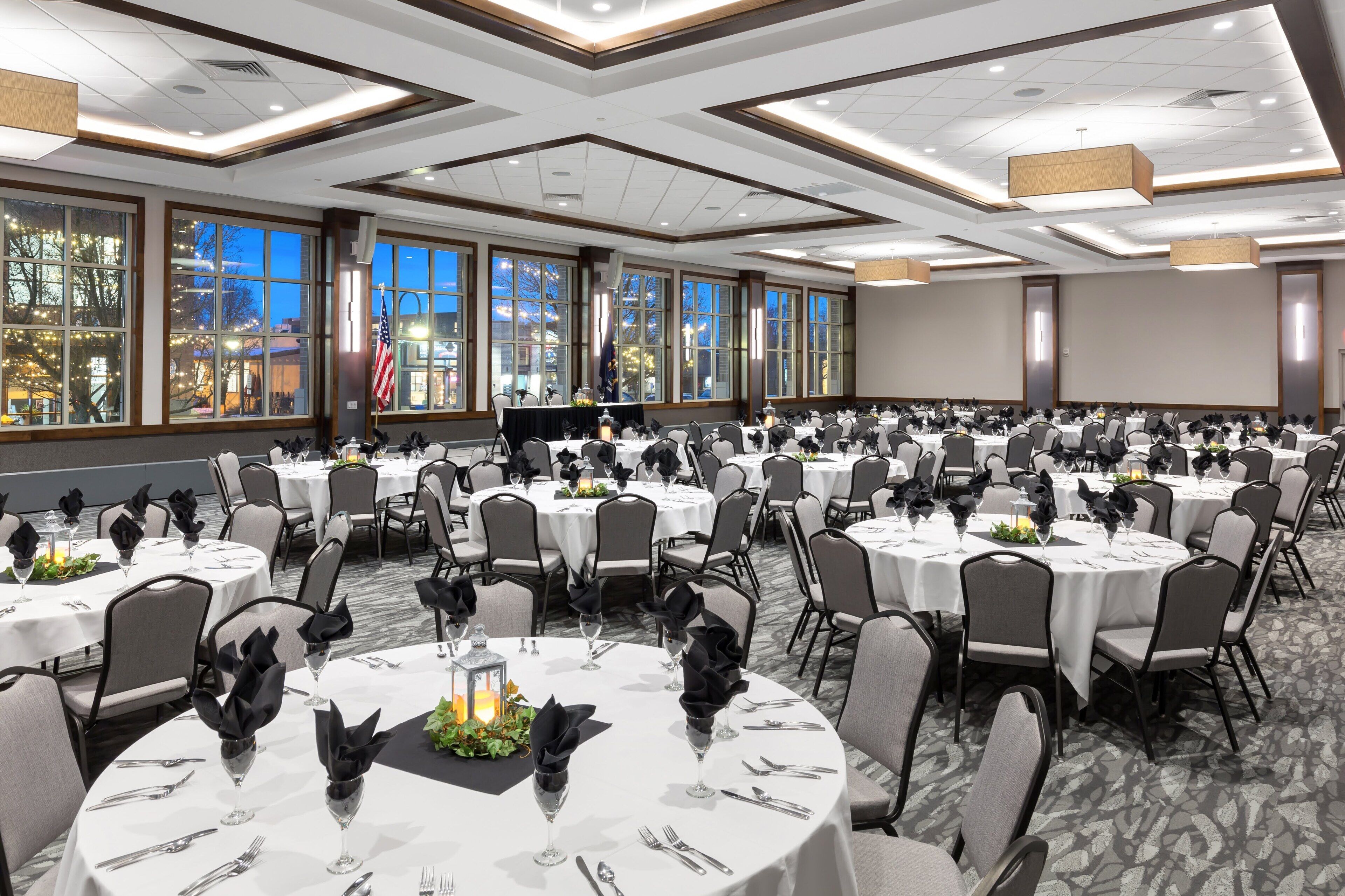 A banquet hall with round tables set for dining, large windows with views, and a flag on the wall.