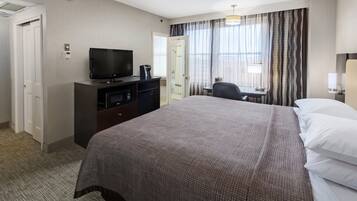 Habitación de hotel con una cama grande, un televisor en una cómoda, un escritorio con una silla y una ventana con cortinas.