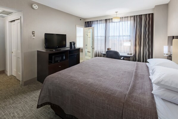 Habitación de hotel con una cama grande, un televisor en una cómoda, un escritorio con una silla y una ventana con cortinas.