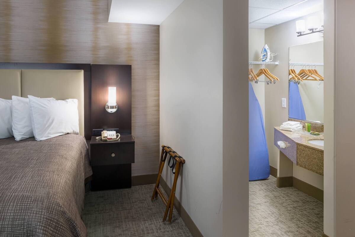 Ein Hotelzimmer mit Bett, Nachttisch, Lampe und Spiegel im Badezimmer.