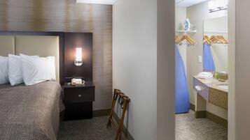 A hotel room with a bed, bedside table, lamp, and a mirror in the bathroom.