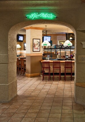 A bar area with a neon sign reading "Minercas," wooden bar stools, and a tiled floor.