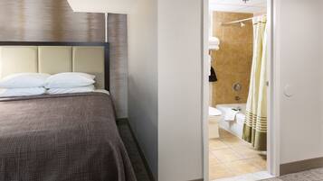 Una habitación de hotel con cama, baño visible a través de una puerta abierta y zona de ducha.