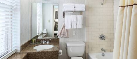 Ein Badezimmer mit Waschbecken, Toilette und Badewanne. Ein Handtuchhalter mit Handtüchern und einer Duschvorhang sind vorhanden.