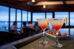 Two martini glasses with a lemon garnish on a bar counter, with a view of the ocean in the background. - Park Place Hotel (Traverse City)