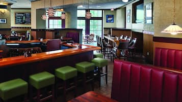 A restaurant with a bar area, booths, and high stools. There are hanging lights and a menu board on the wall.