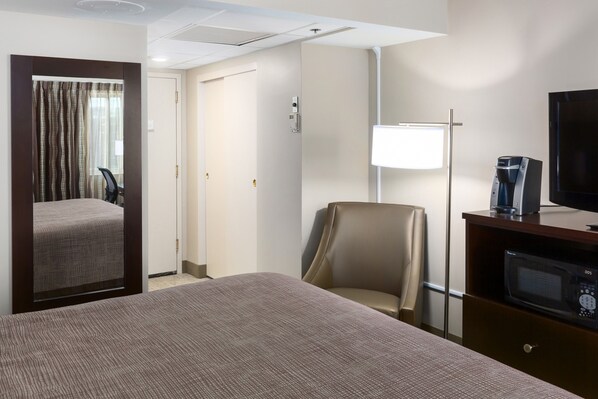A hotel room with a bed, a chair, a desk with a coffee maker, and a television. - Park Place Hotel (Traverse City)
