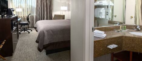 A hotel room with a bed, desk, TV, and a bathroom with a sink and mirror.