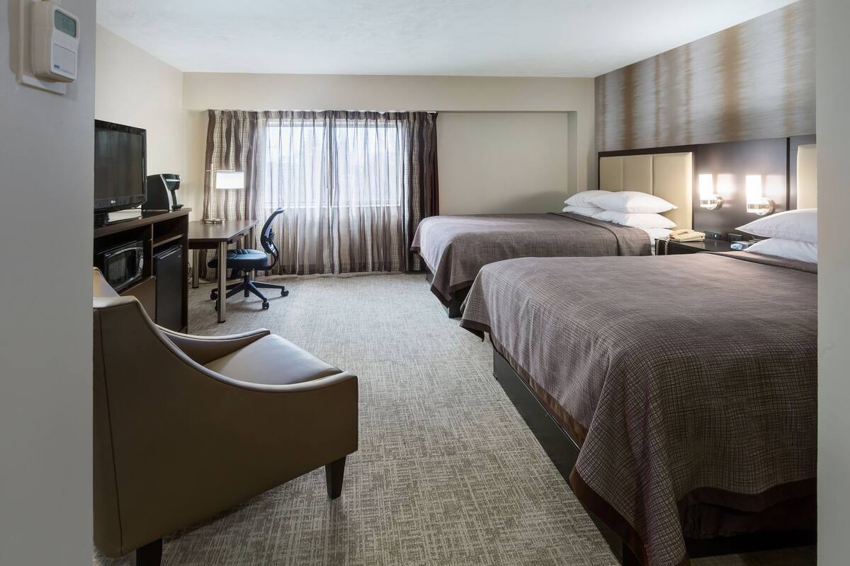 Ein Hotelzimmer mit zwei Betten, einem Schreibtisch mit Computer, einem Stuhl und einem Fernseher.