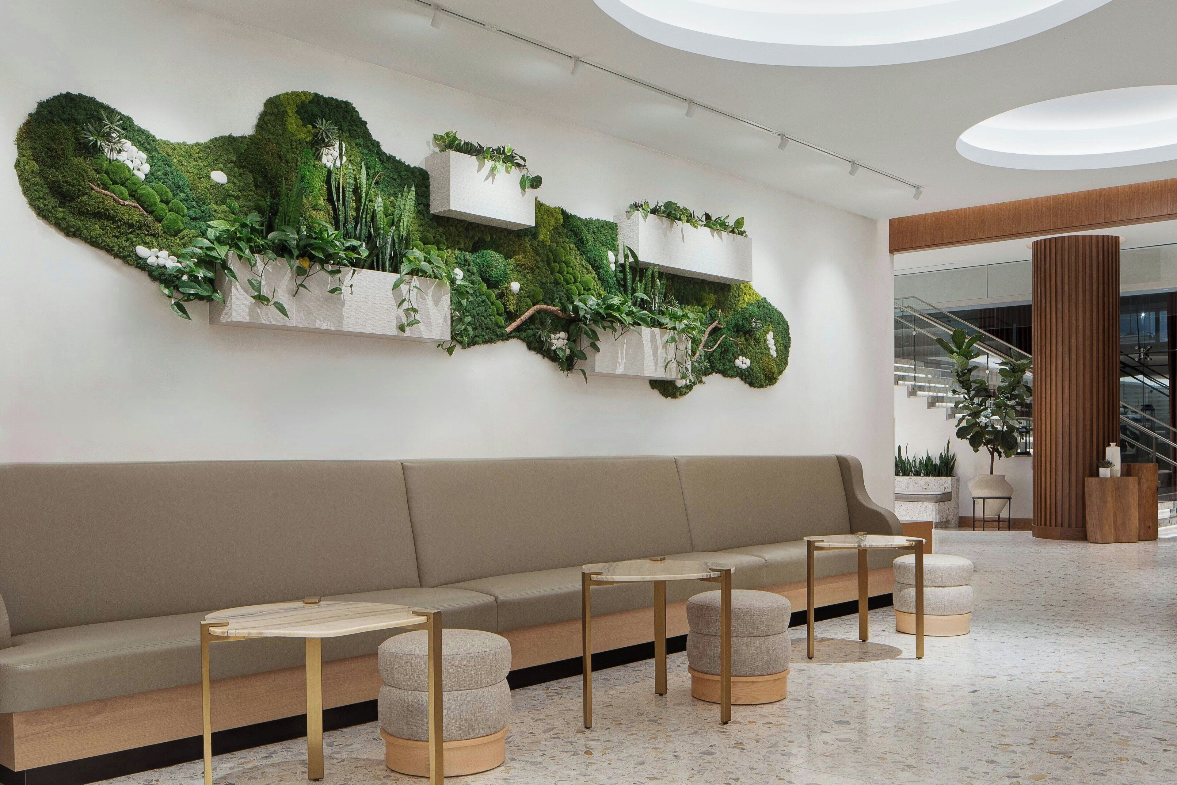 A modern lobby with a green wall installation, a beige sofa, and round ottomans with gold legs.