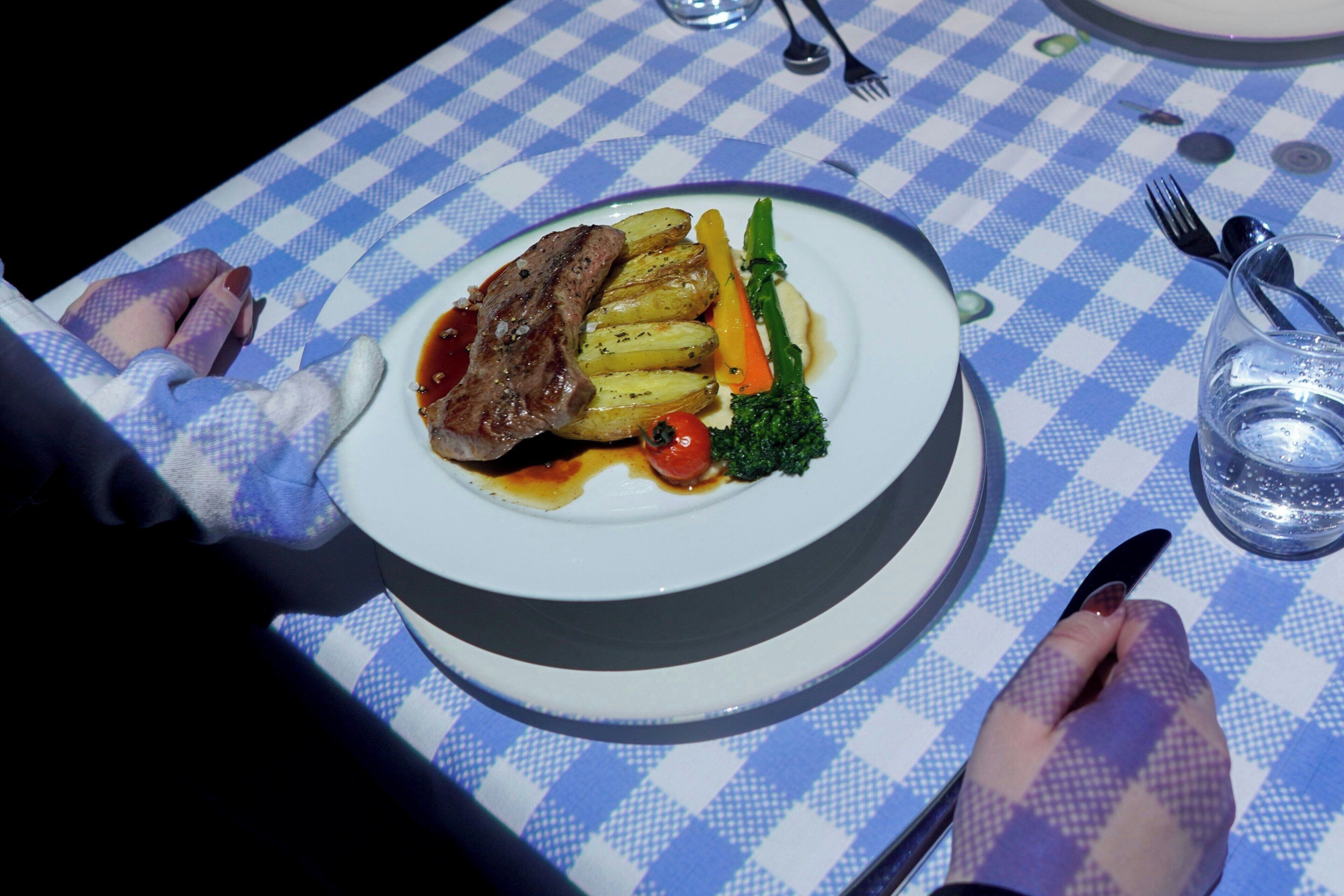 Een tafel met een geruit tafelkleed, een bord eten en bestek.