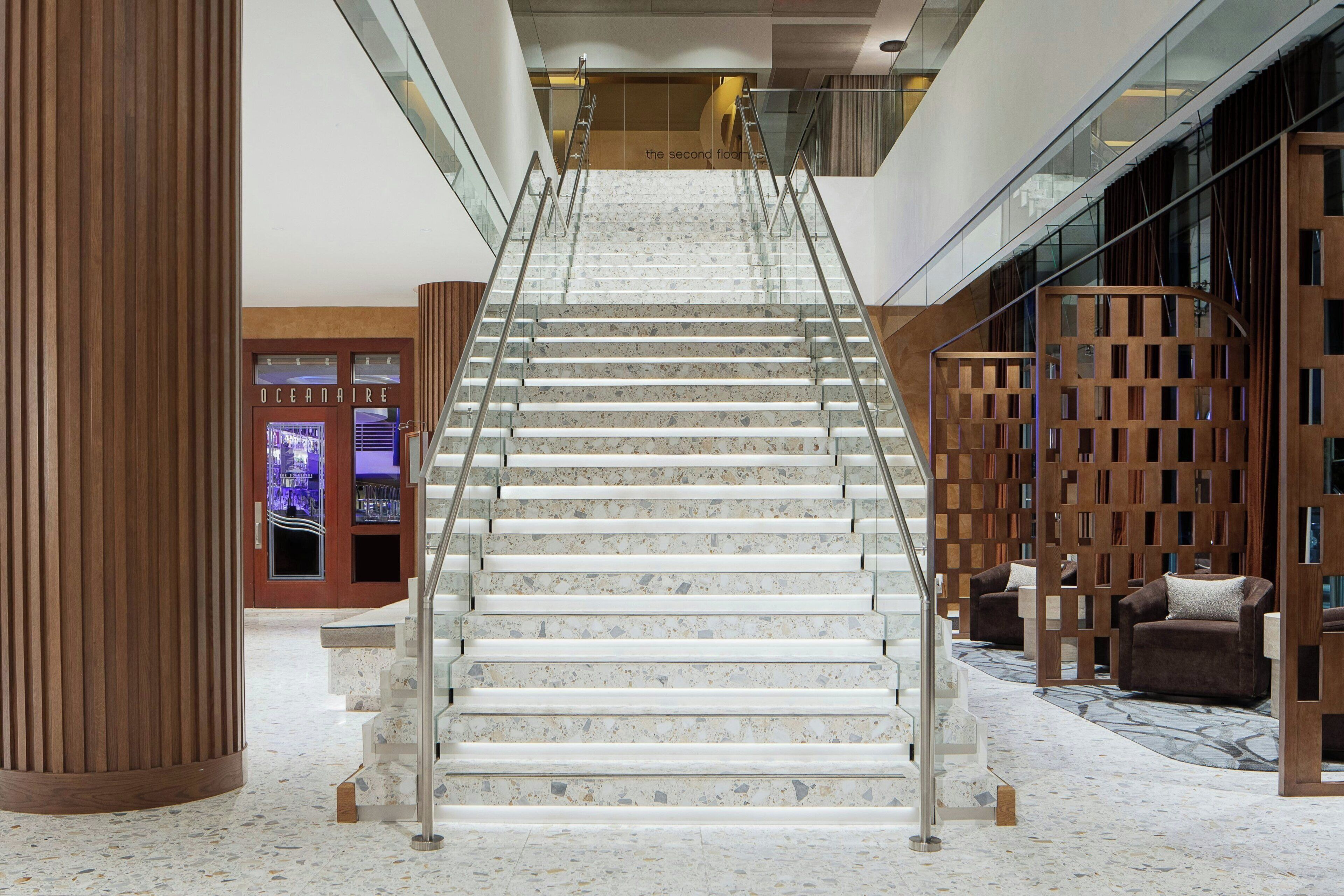 Una escalera de mármol con barandillas de vidrio que conduce a un segundo piso.