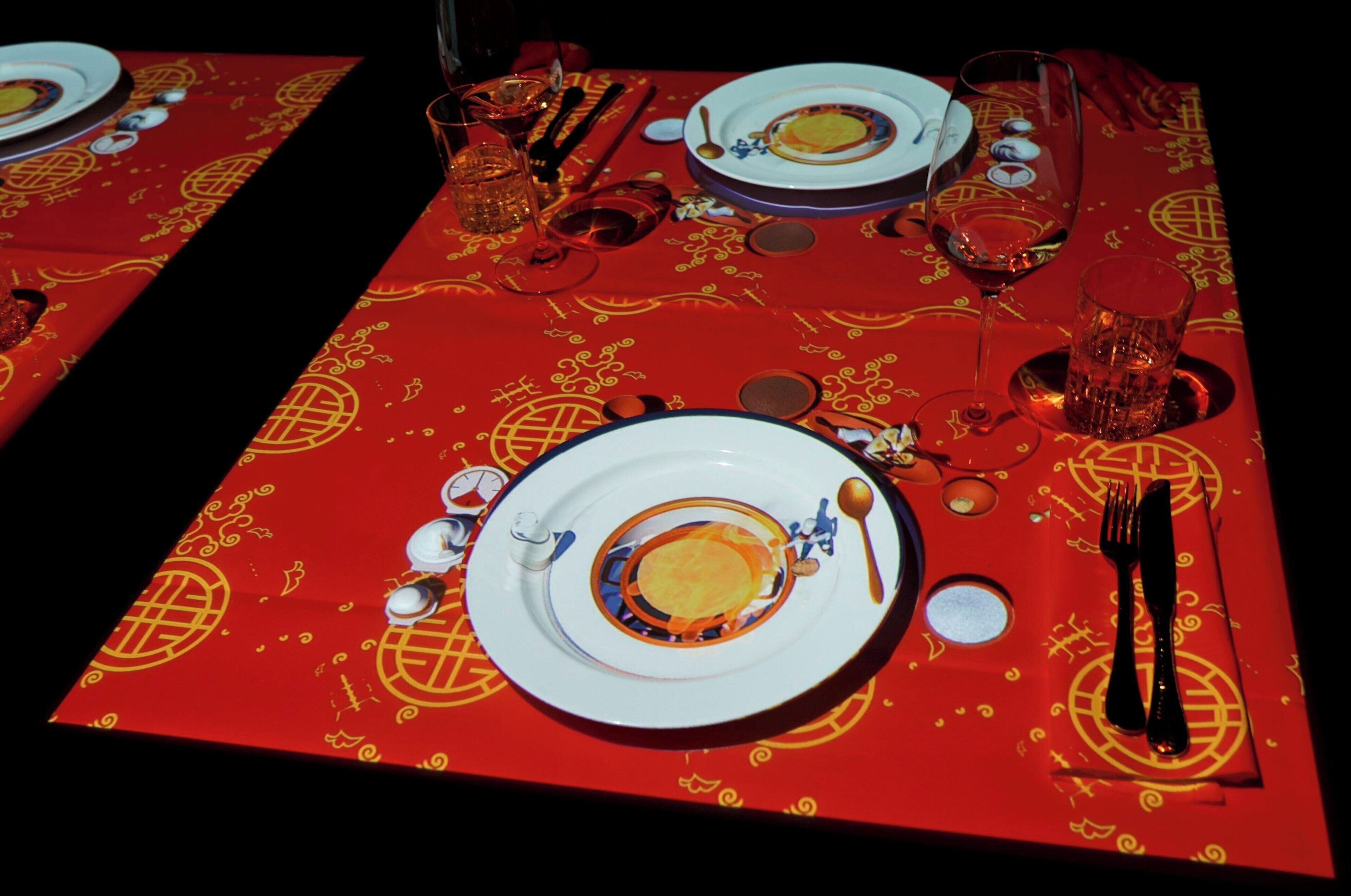 Una mesa dispuesta con platos, vasos y cubiertos, cubierta por un mantel rojo con diseños dorados.