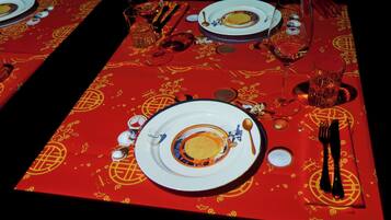 Una mesa dispuesta con platos, vasos y cubiertos, cubierta por un mantel rojo con diseños dorados.