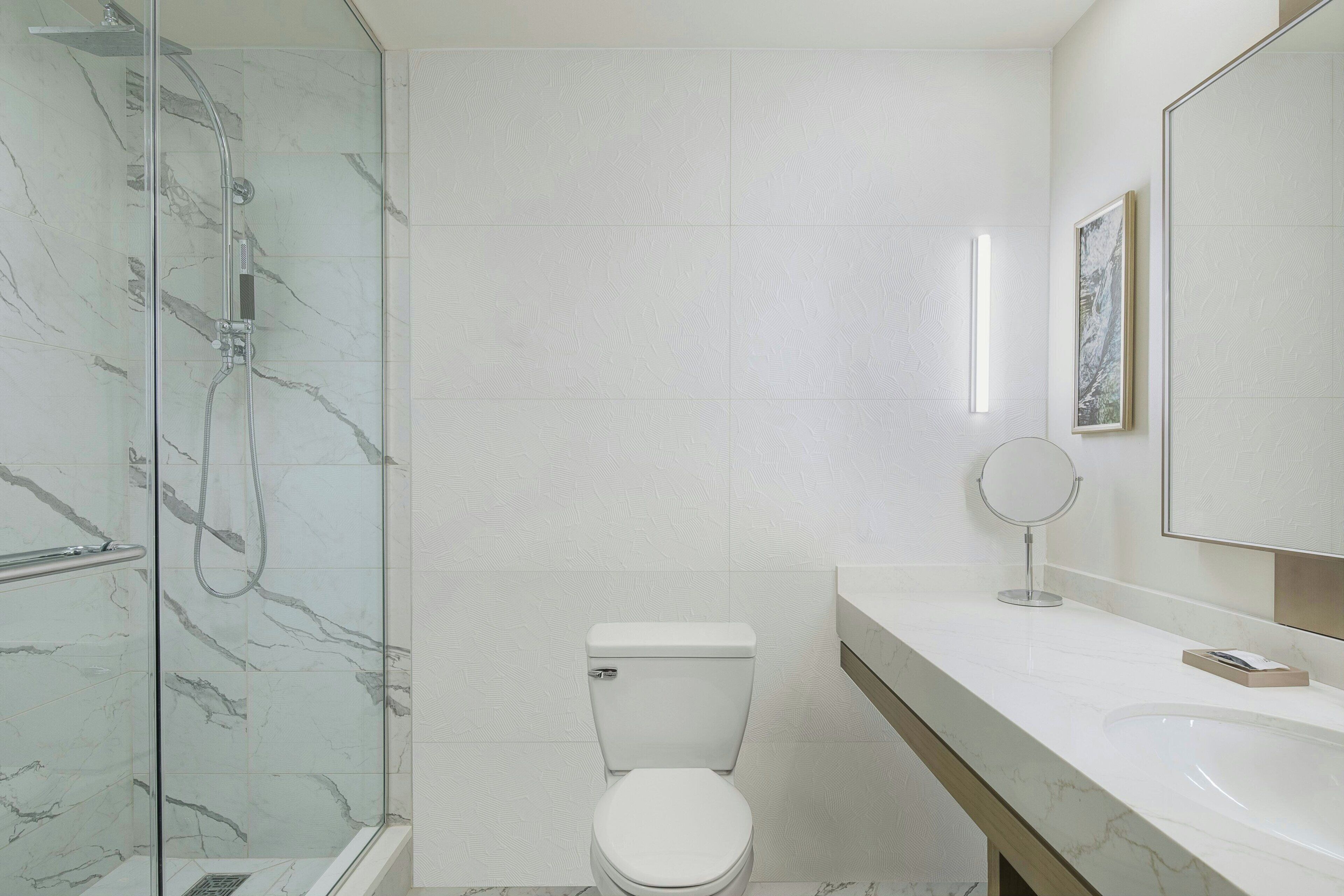 Un baño moderno con ducha envuelta en vidrio, inodoro blanco y un espejo grande sobre un lavabo blanco.