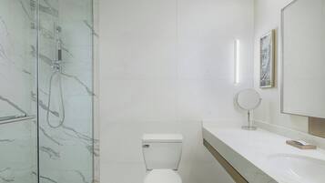 Un baño moderno con ducha envuelta en vidrio, inodoro blanco y un espejo grande sobre un lavabo blanco.