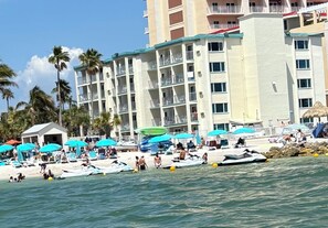 A beachfront hotel with multiple balconies, a pool area, and beach umbrellas.