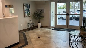 A reception area with a marble floor, a reception desk, a potted plant, a chandelier, and a view of parked cars through the glass doors.