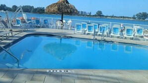 A pool area with clear blue water, white lounge chairs, and a thatched umbrella.
