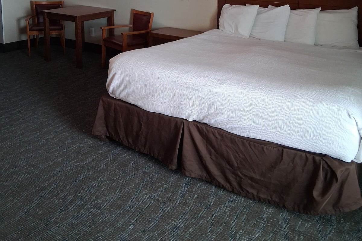 Ein Hotelzimmer mit einem großen Bett, einem Schreibtisch mit zwei Stühlen, einer Lampe und einem Bild einer Strandlandschaft.