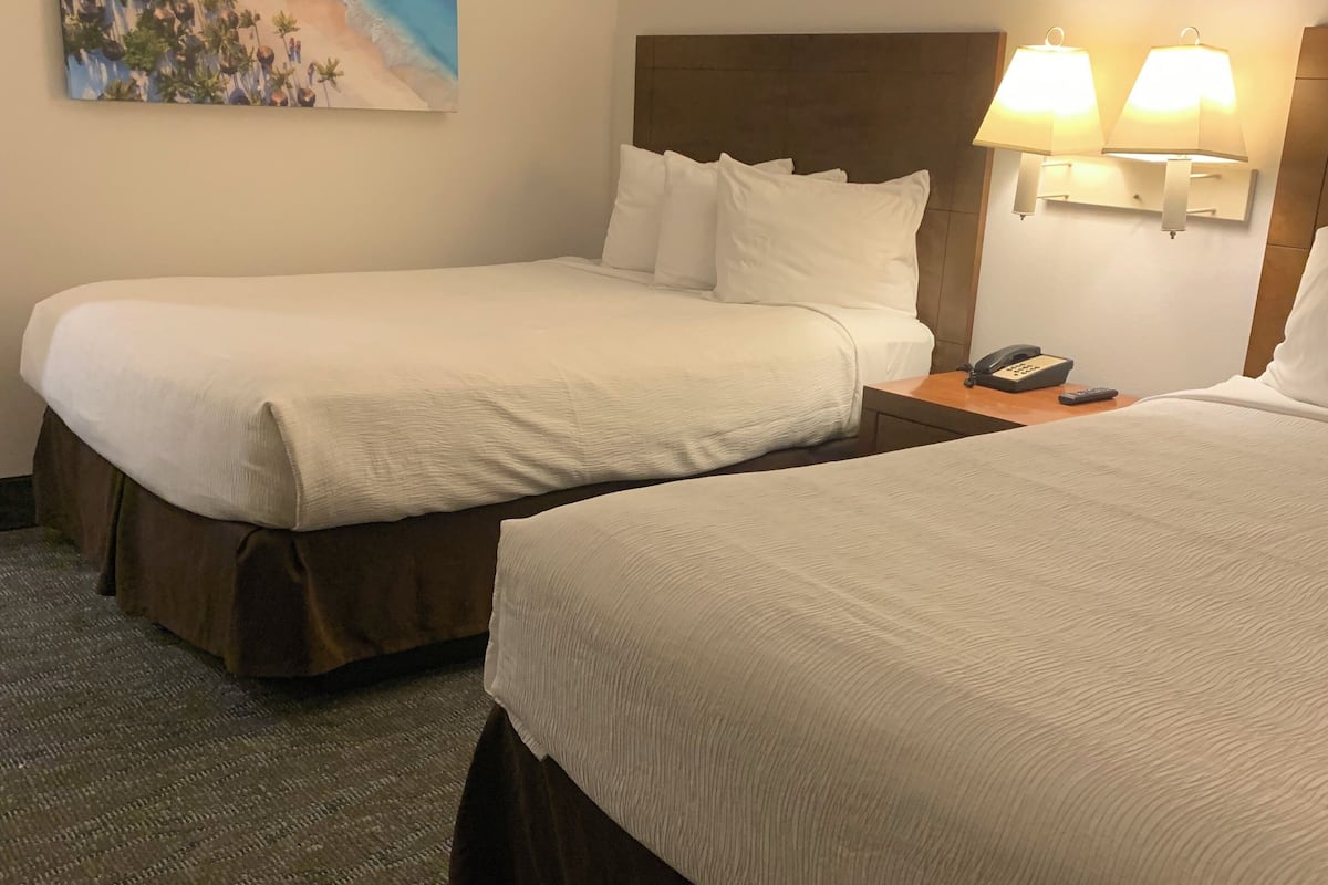 Ein Hotelzimmer mit zwei Betten, einem Strandbild, einem Nachttisch mit Lampe und einem Telefon.