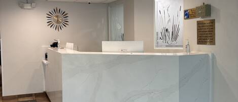 A reception area with a marble counter, a clock, a door, and a sign on the wall.