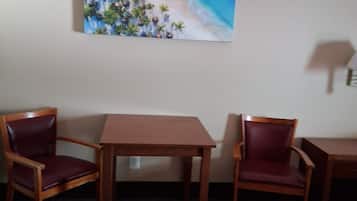 Una habitación con una mesa de madera y dos sillas, un cuadro de una escena de playa en la pared, y una lámpara en el lado derecho.
