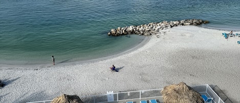 A beach with a pool, lounge chairs, and a lifeguard tower.