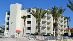 A multi-story hotel with balconies, palm trees, and a red umbrella.