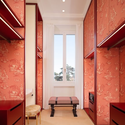 A room with a large window, a bench, and red patterned walls.
