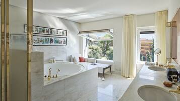 A modern bathroom with a large bathtub, two sinks, and a large window offering a view of greenery and buildings.