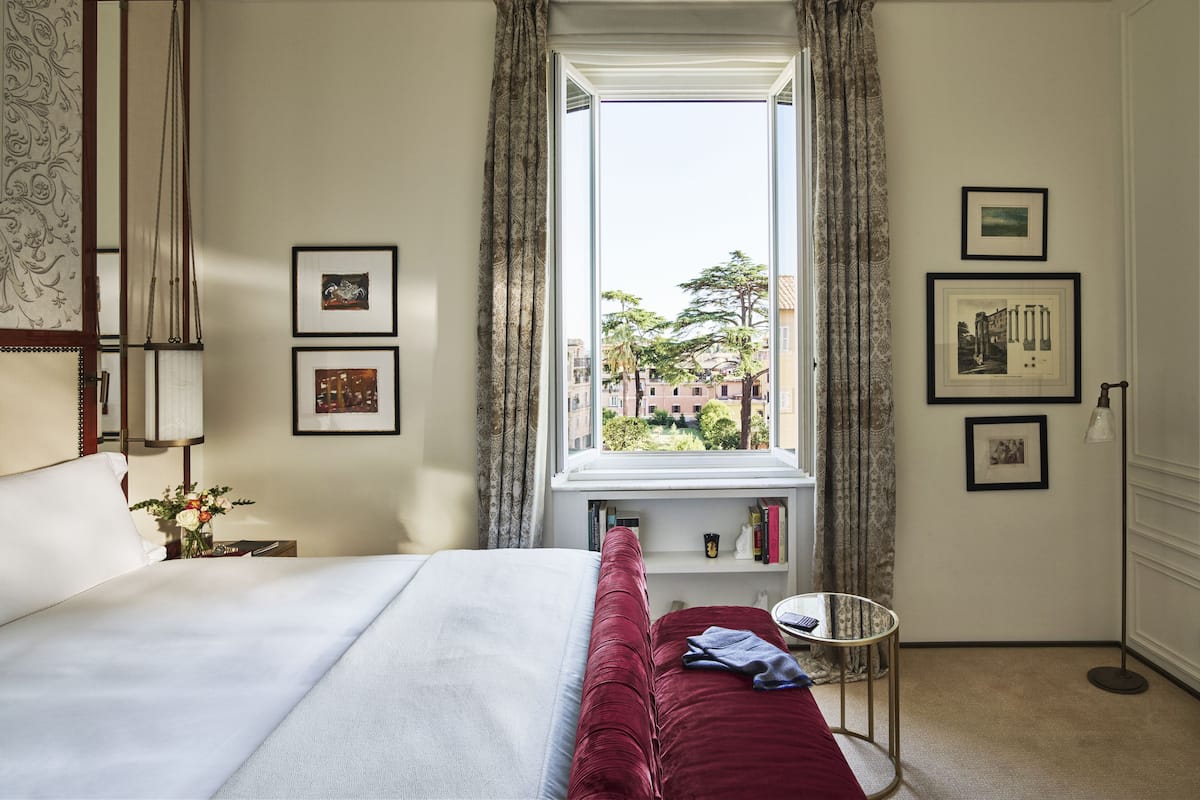 Habitación de hotel con una cama grande, ventana con cortinas, cuadros en la pared y una mesita redonda.