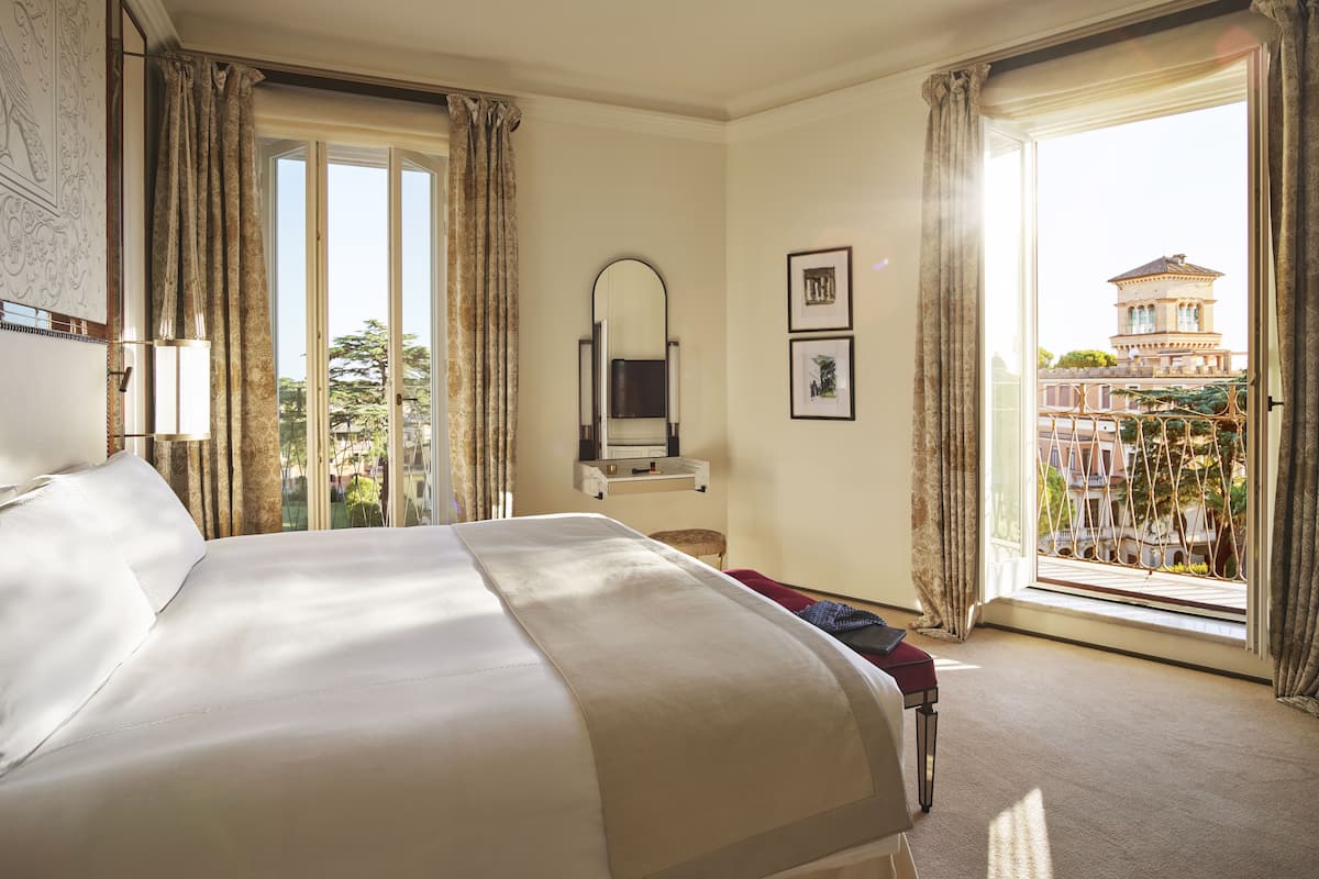 Habitación de hotel con una cama grande, un escritorio, un televisor y un balcón con vistas a un edificio.