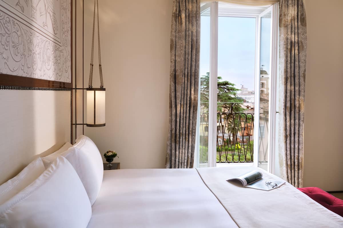 Habitación de hotel con una cama grande, una mesita de noche con lámpara y vistas a un edificio a través de la ventana.