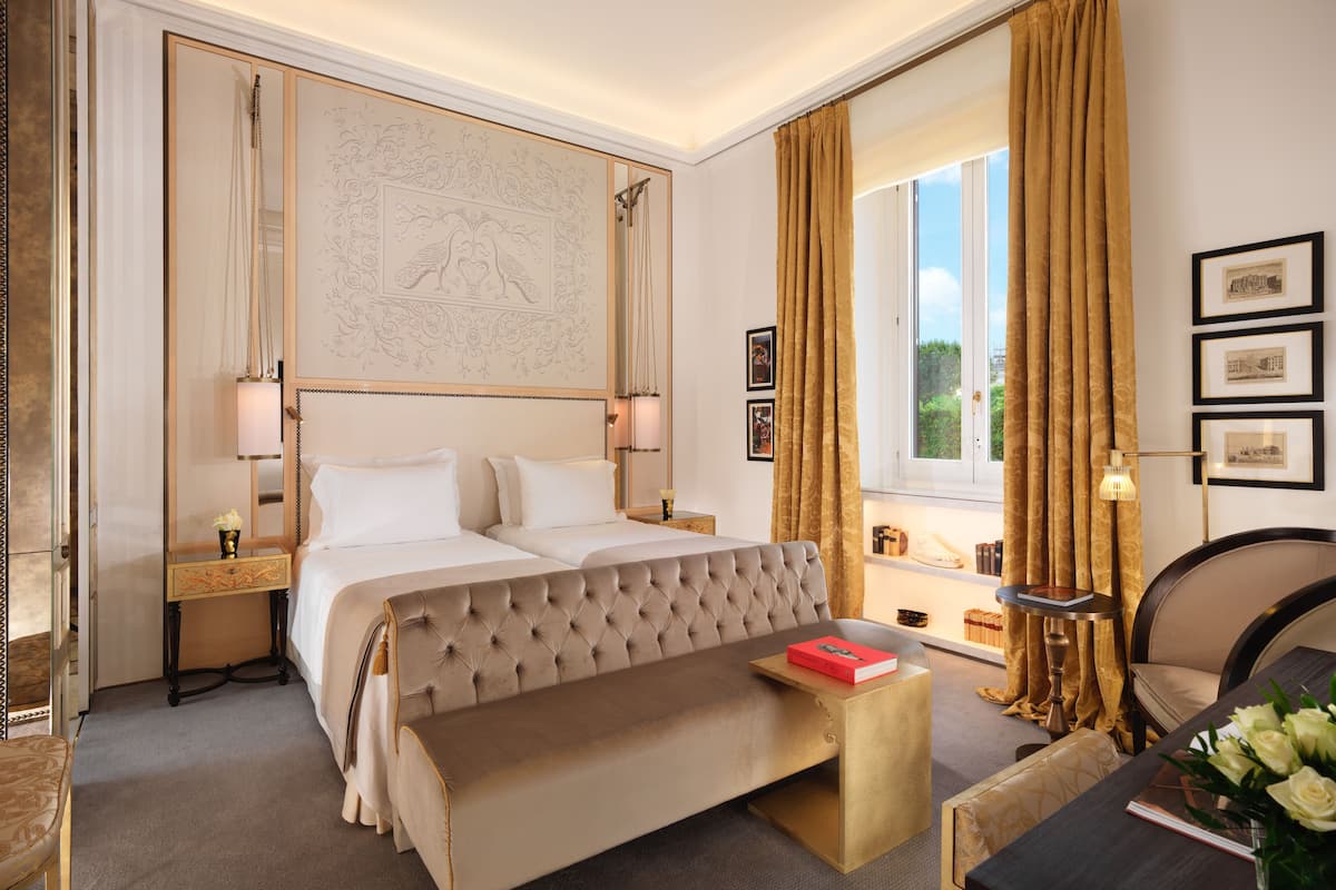 Habitación de hotel con una cama grande, un banco, un escritorio y una ventana con cortinas.