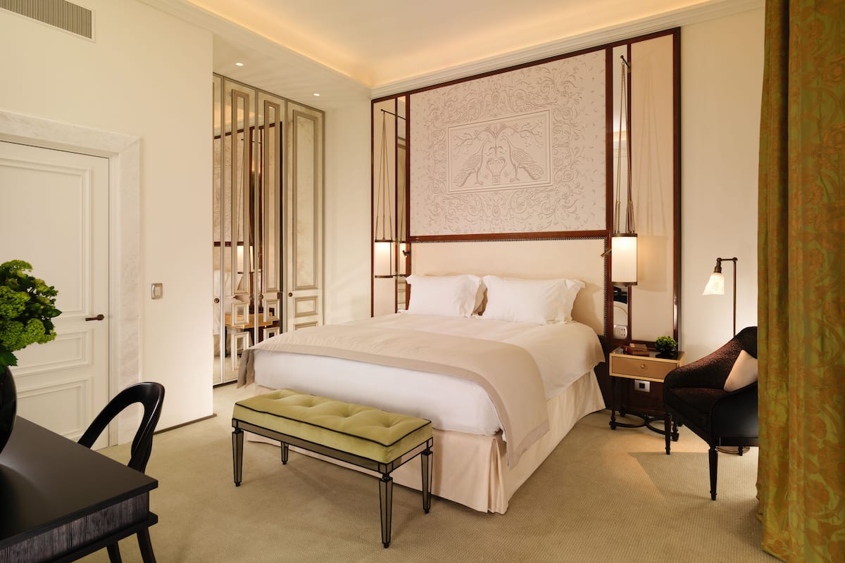 Una habitación de hotel con una cama grande, un banco, un escritorio y una silla.