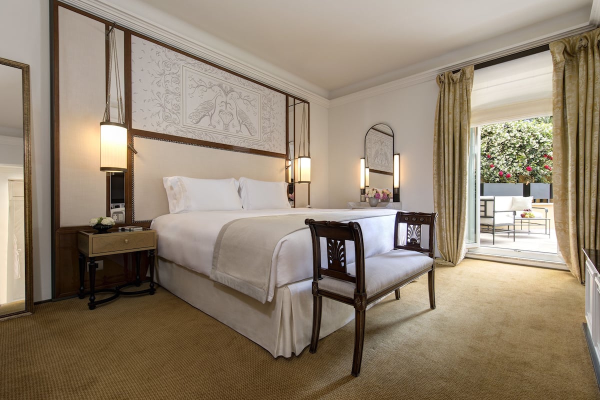 Habitación de hotel con una cama grande, una mesita de noche, una silla, un espejo y vistas al exterior.