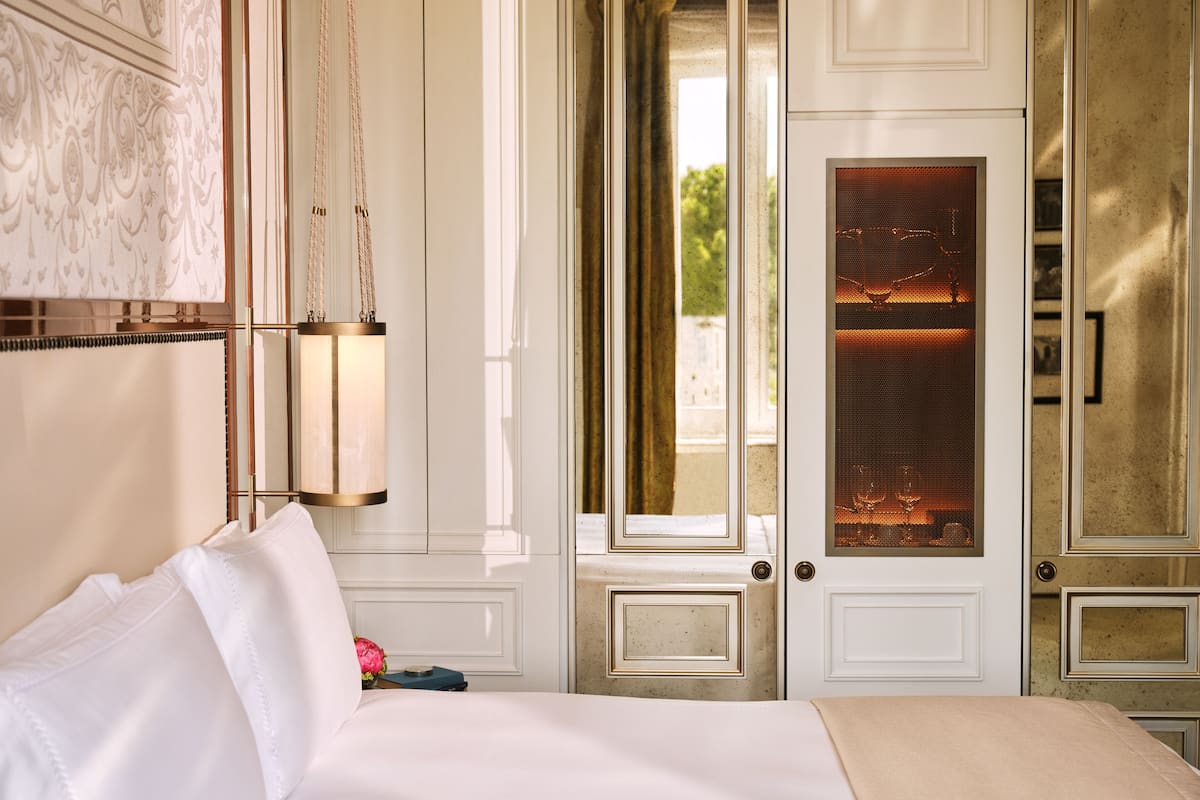 Habitación de hotel con una cama, lámpara colgante, puerta con panel de vidrio esmerilado y vistas al exterior.
